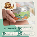 Hand holding a container of Green Milk Calming Baby Rub with key benefits listed below.