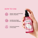 Hand holding a Green Milk Pannir Rose Face Mist with usage instructions on a pink background